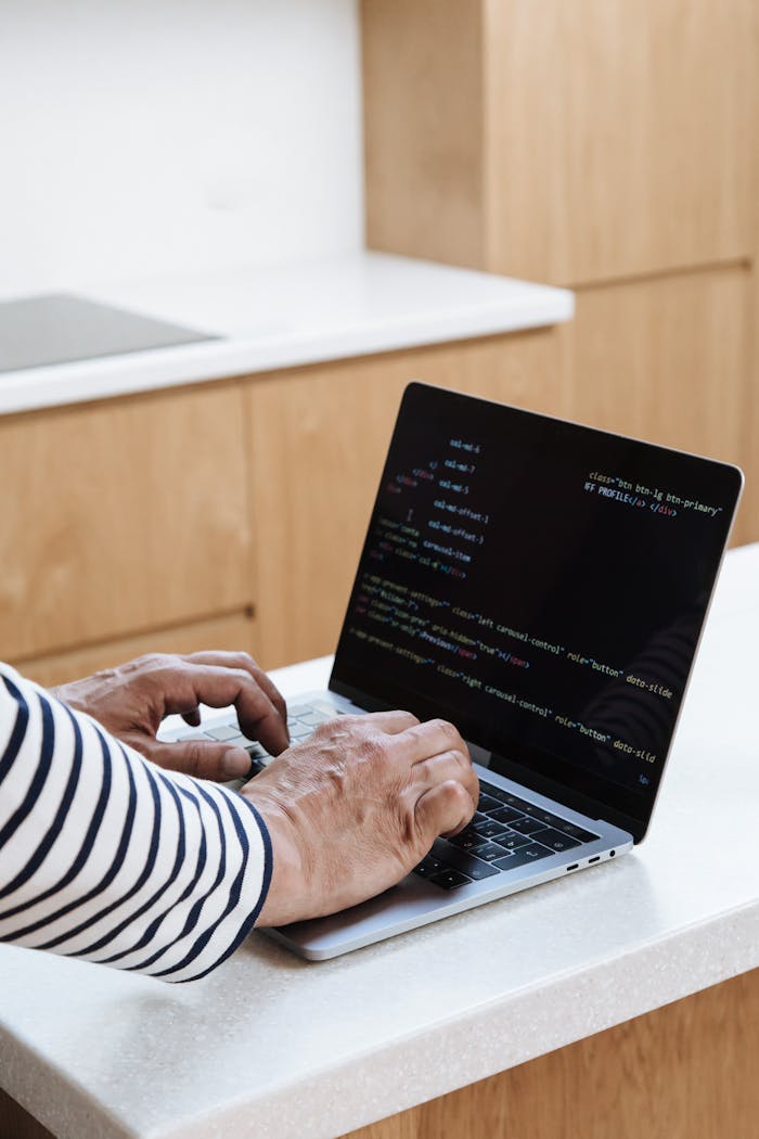 Close-up of senior adult programming on a laptop in a modern kitchen setting.